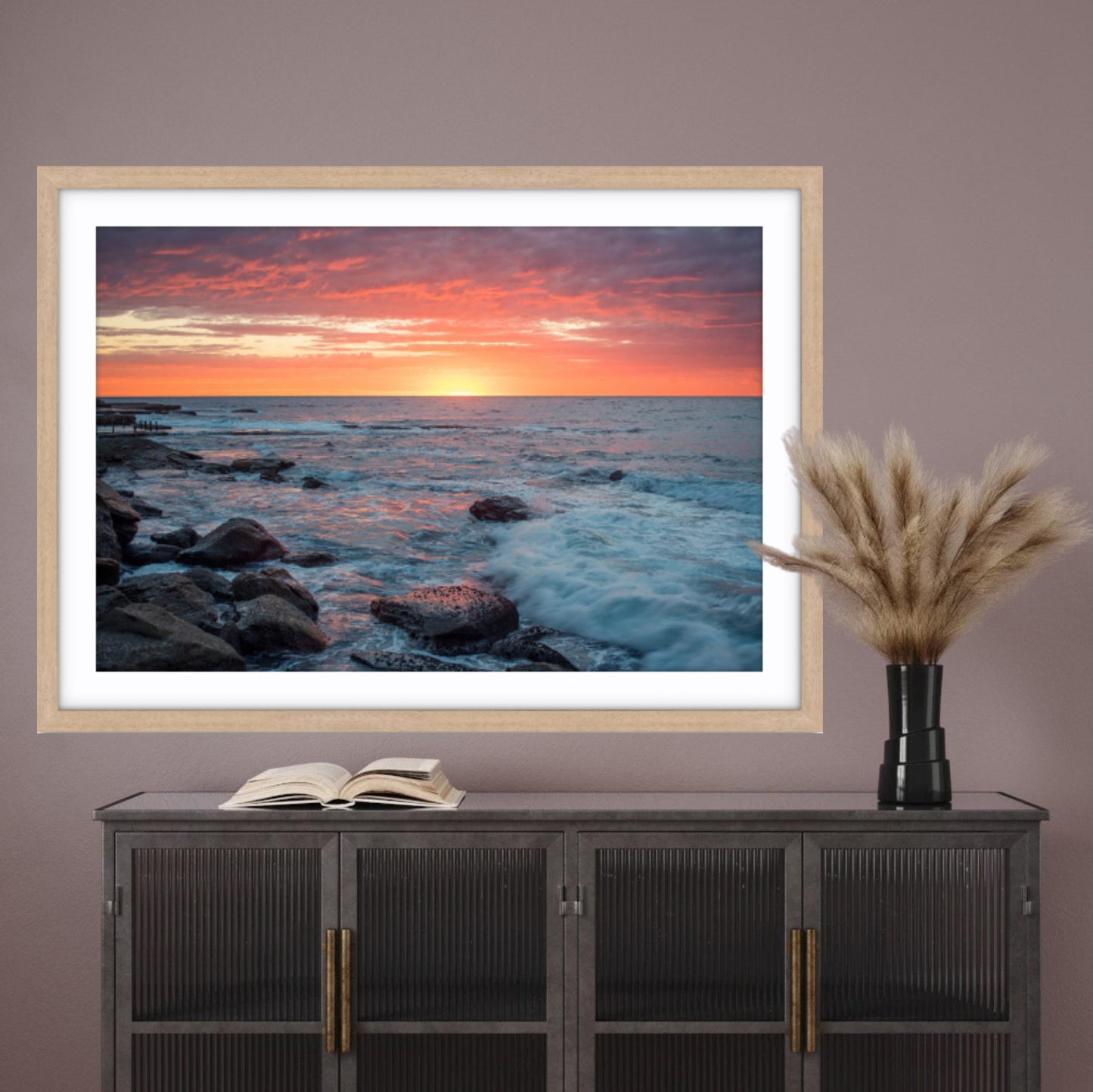 Framed fine art photograph of a sunrise at Maroubra Beach on a wall above a cabinet with decor items.