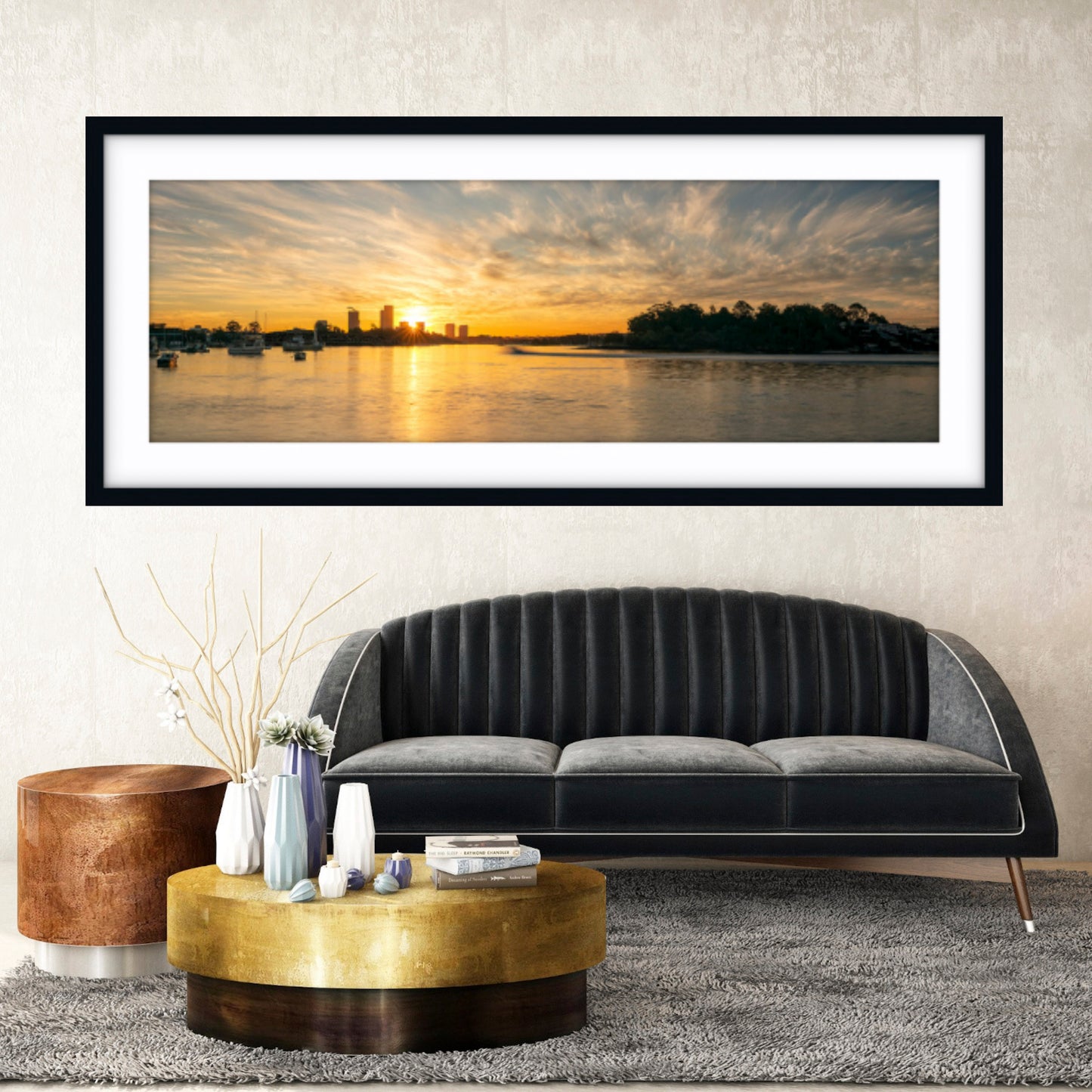 Framed sunset over water artwork above a black sofa in a living room.