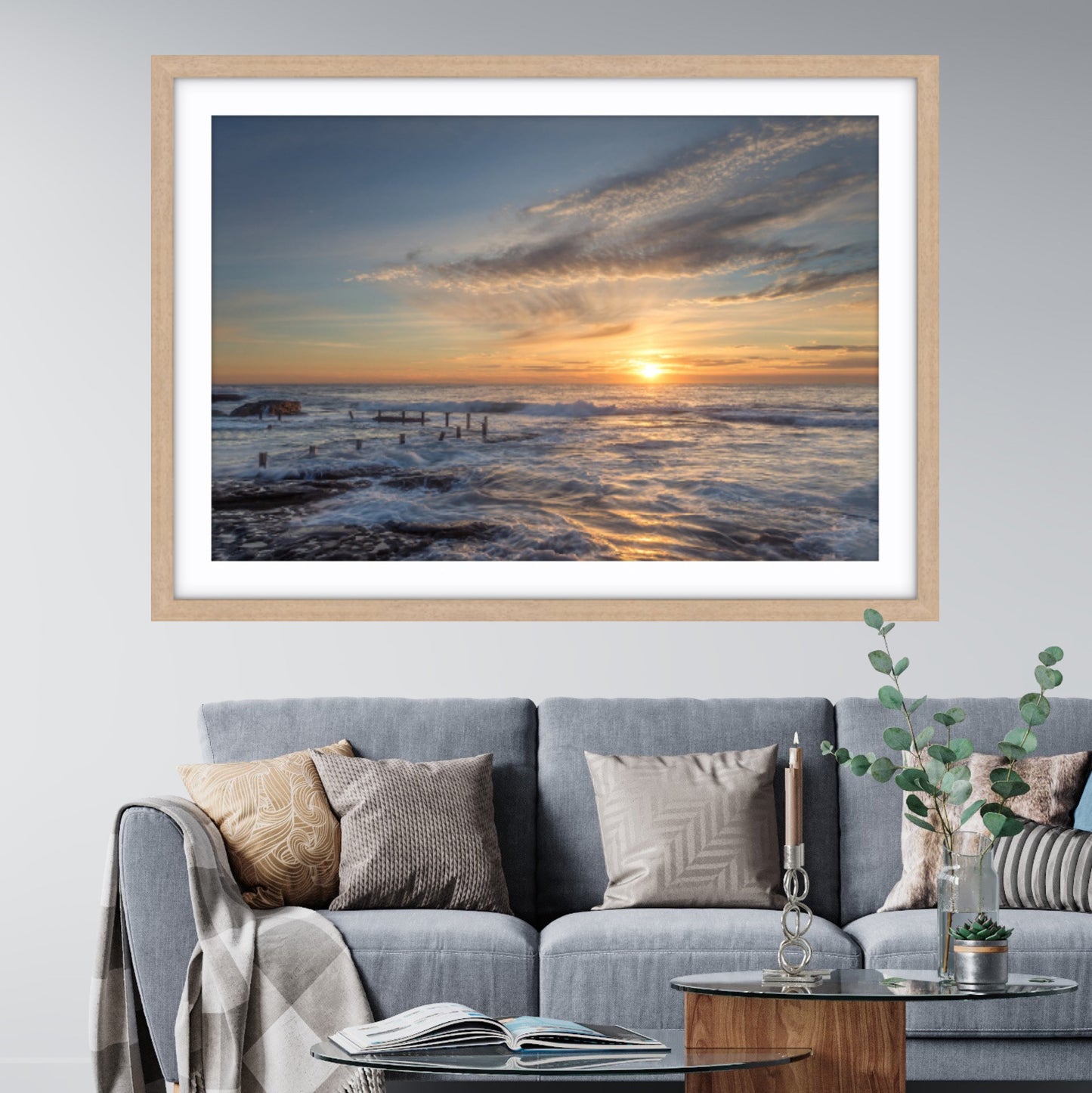 Framed beach sunrise art at Maroubra above a gray sofa in a living room.