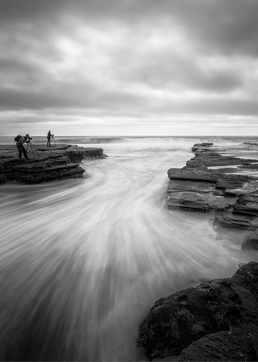 Black and white long exposure photograph of photographers at Turimetta Beach dawn with rocky coastline Northern Beaches Sydney