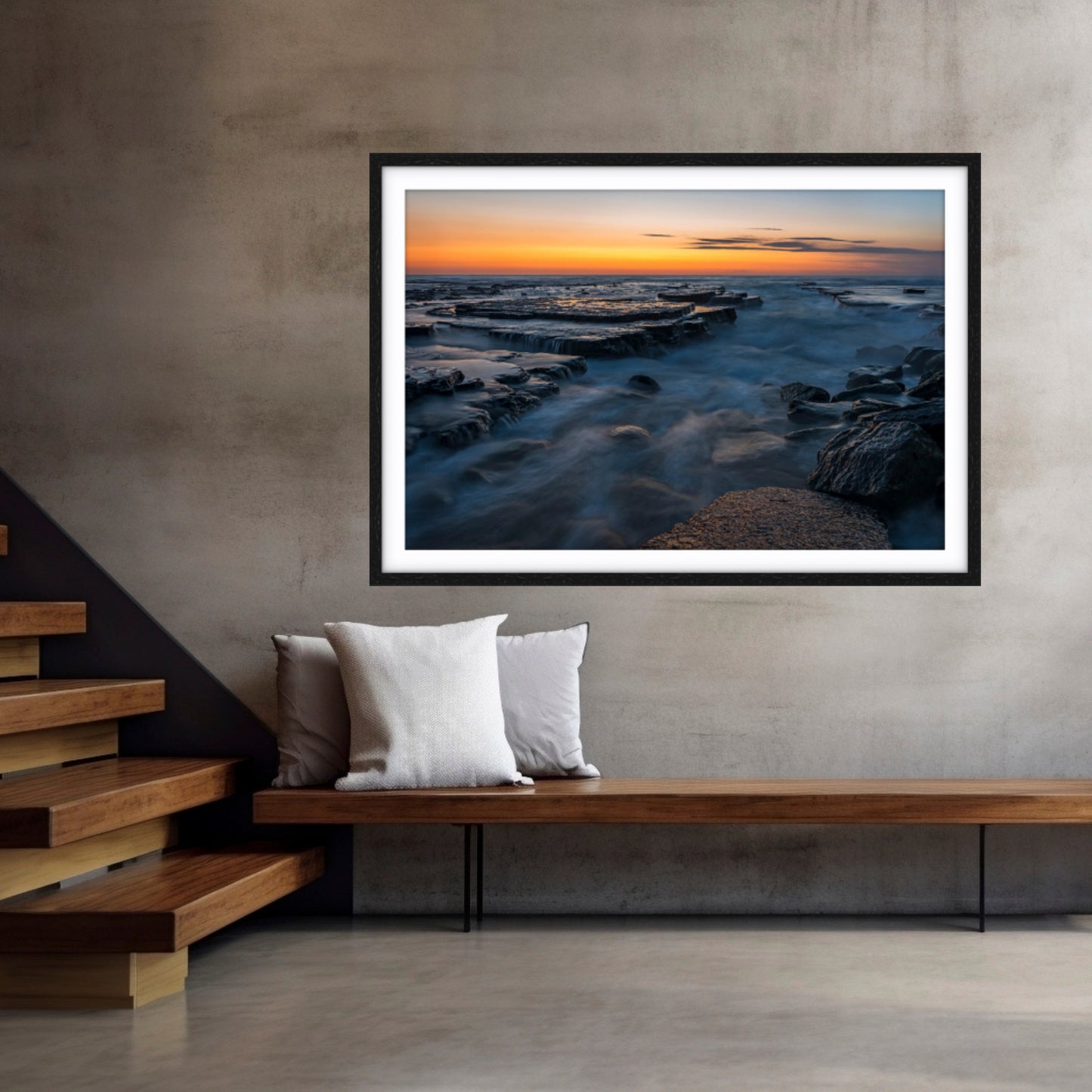 Framed fine art photographic print of a sunrise at Turimetta Beach, Northern Beaches on a wall above a wooden bench.