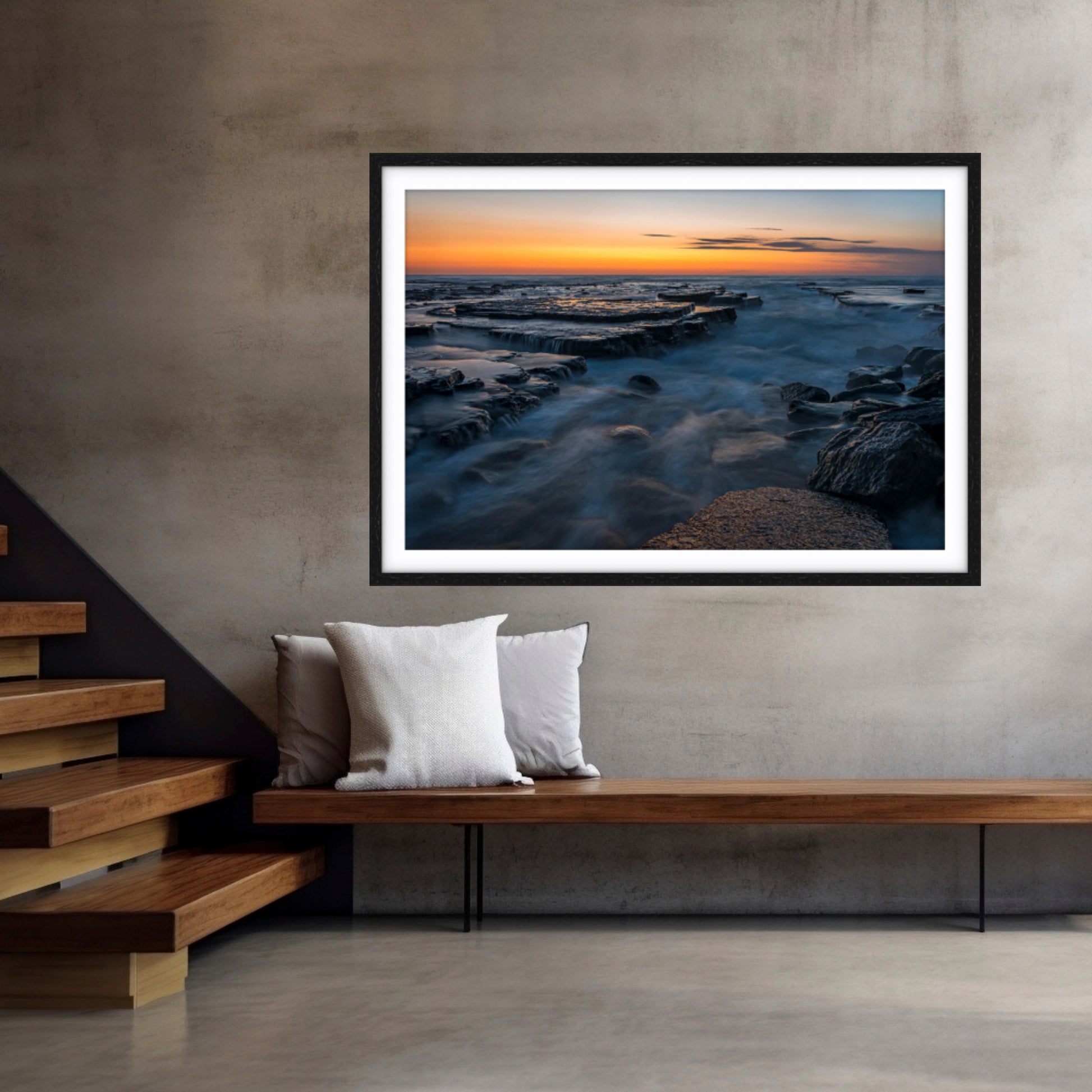 Framed fine art photographic print of a sunrise at Turimetta Beach, Northern Beaches on a wall above a wooden bench.