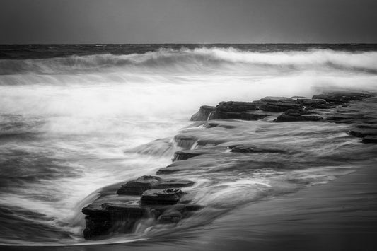 Black and white long exposure photograph of rocky ledge with receding water at Turimetta Beach Sydney Northern Beaches