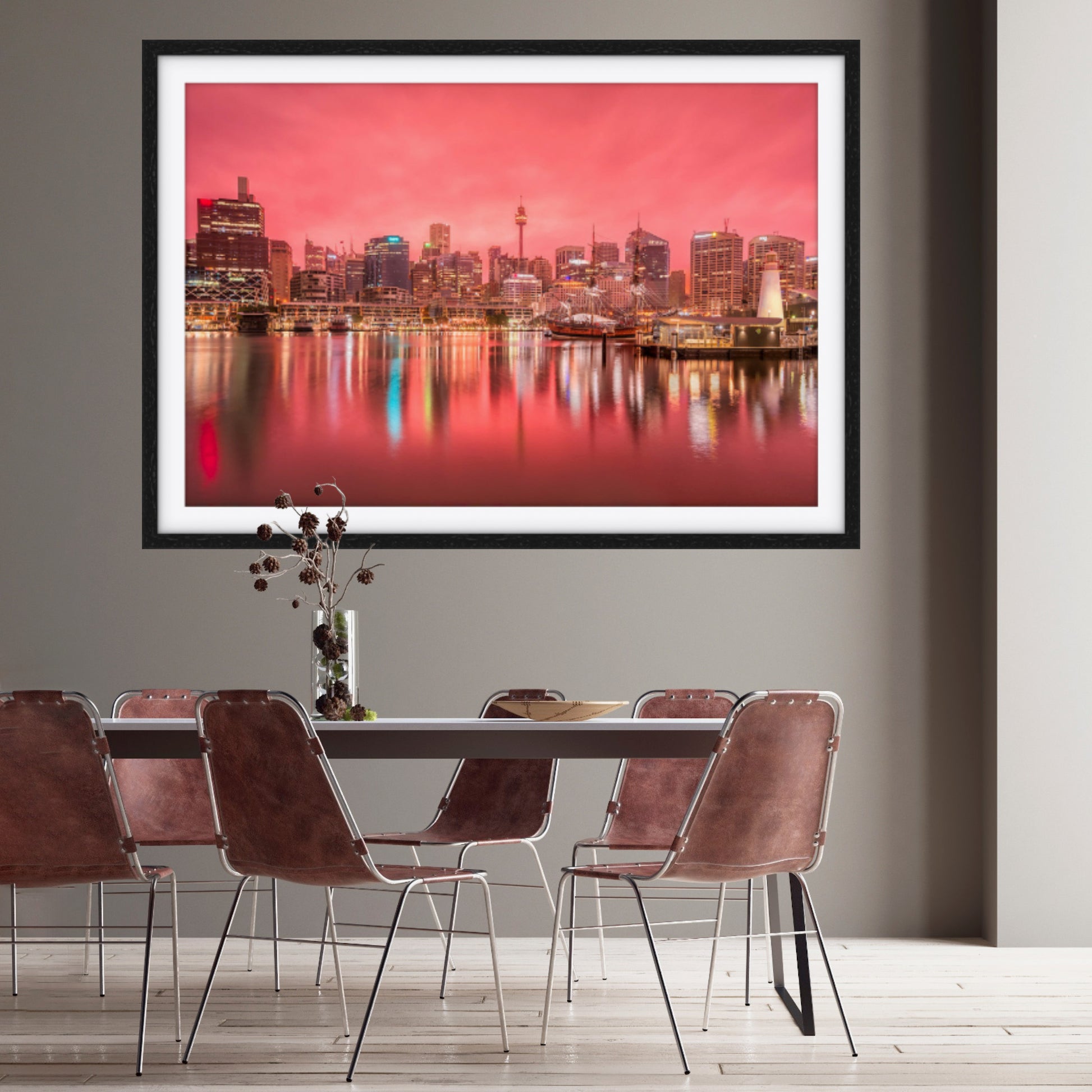 Framed cityscape print in rose pink on a wall above a dining table with chairs.