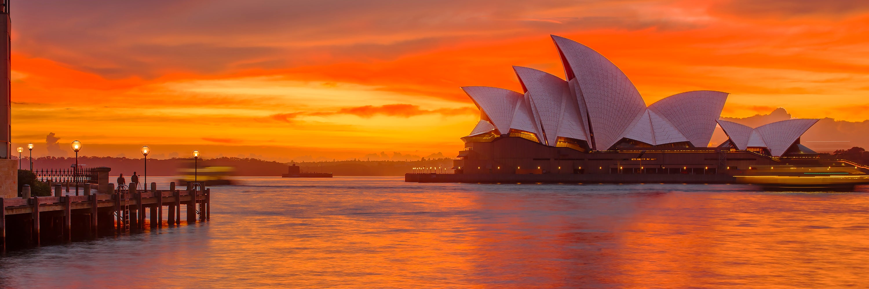 Color long exposure photograph of Sydney Opera House Circular Quay amber yellow light before sunrise two ferries crossing paths