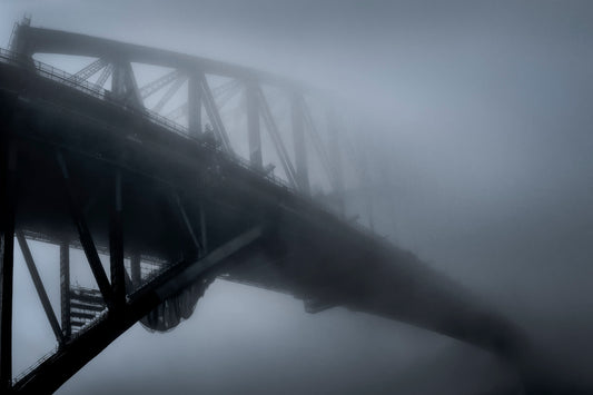Black and white photograph of Sydney Harbour Bridge partially obscured by dense fog at dawn winter morning
