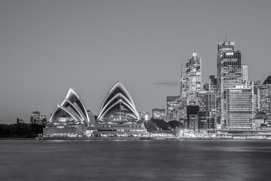 Black and white long exposure panoramic photograph of Sydney Opera House at dusk with smooth harbour water reflections