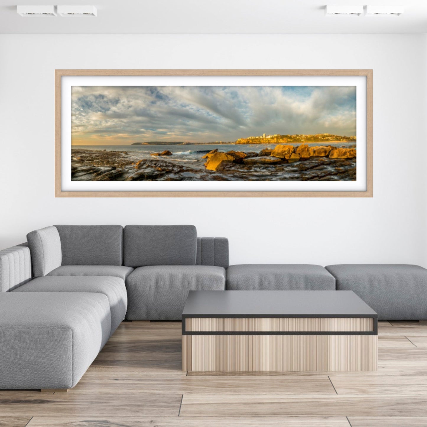 A large framed coastal photograph on the wall, with a gray sofa in a living room. 