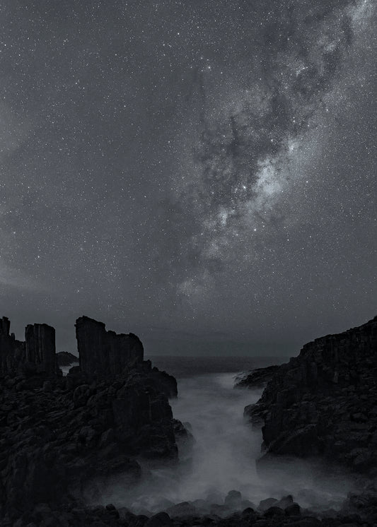 Black and white astrophotography of Milky Way over coastal rocks with ethereal breaking waves long exposure Kiama NSW South Coast