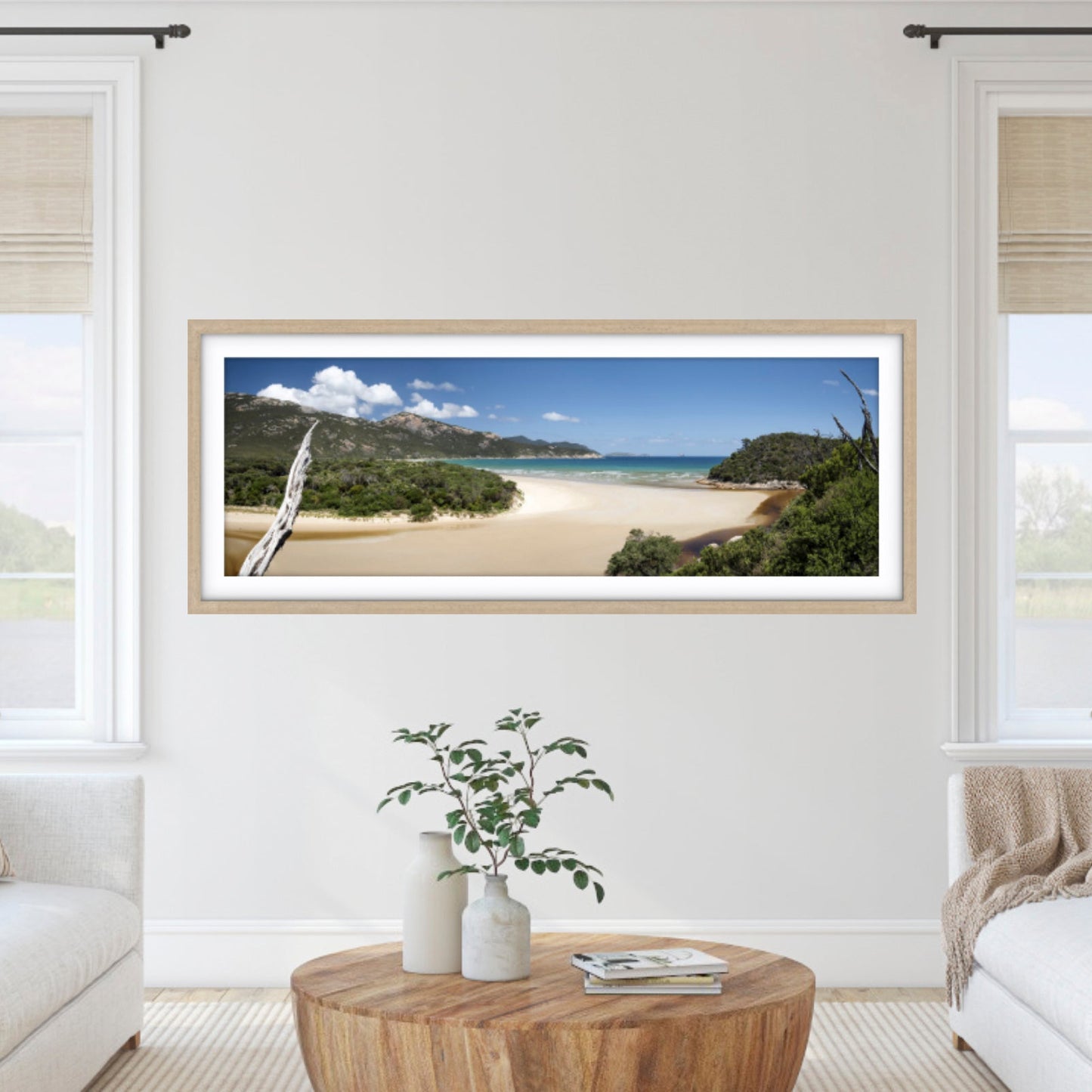 Framed beachscape photography print on a wall in a living room with white walls and furniture.