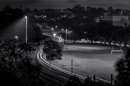Black and white long exposure photograph of Sydney light rail trails through Pyrmont harbourside park at dusk