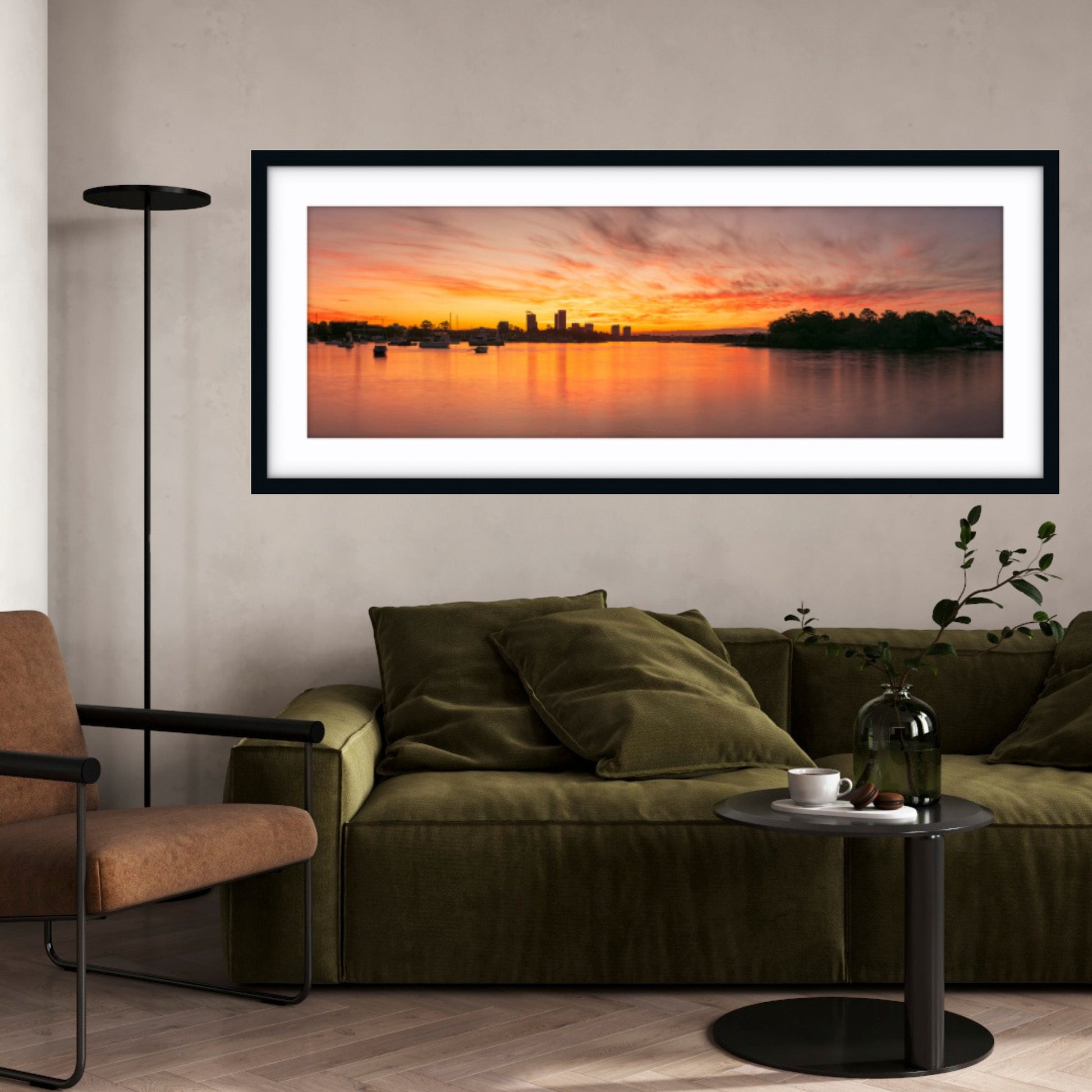 Framed artwork of a sunset over water hanging on a wall above a sofa.