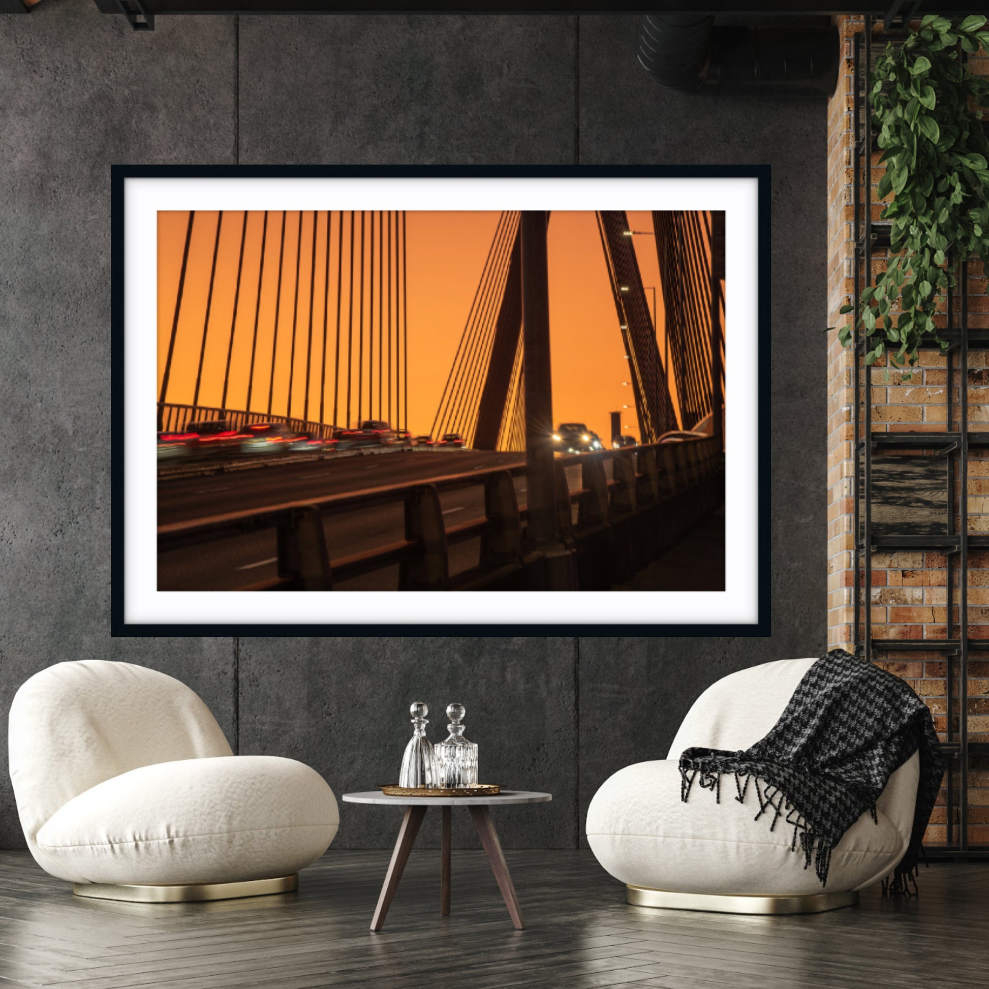 Framed fine art photograph of a Anzac Bridge at sunset hanging on a dark wall above two white chairs.