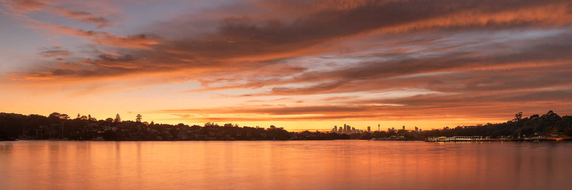 Color long exposure photograph of graceful cloud formation over Parramatta River glasslike water pre-dawn Sydney CBD distance Breakfast Point