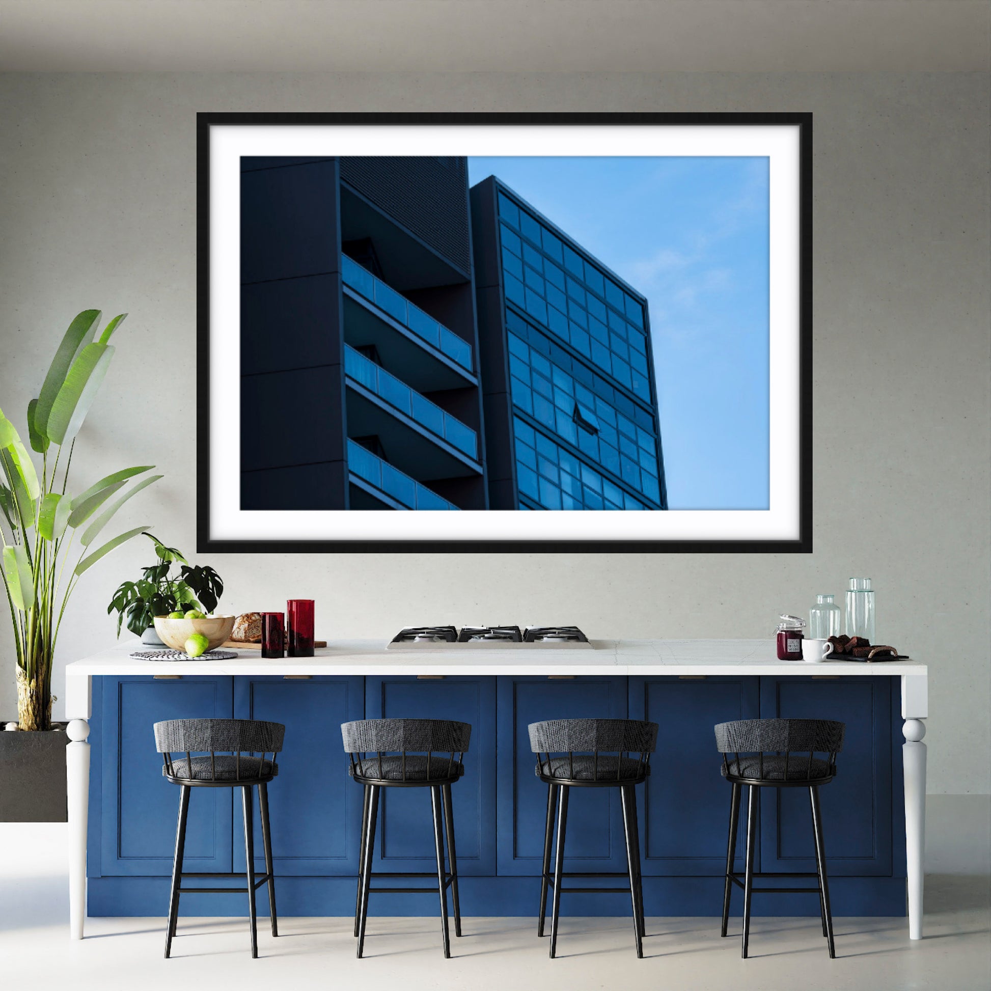 Framed fine art abstract architectural photograph with blue tones on a wall above a kitchen counter with stools.