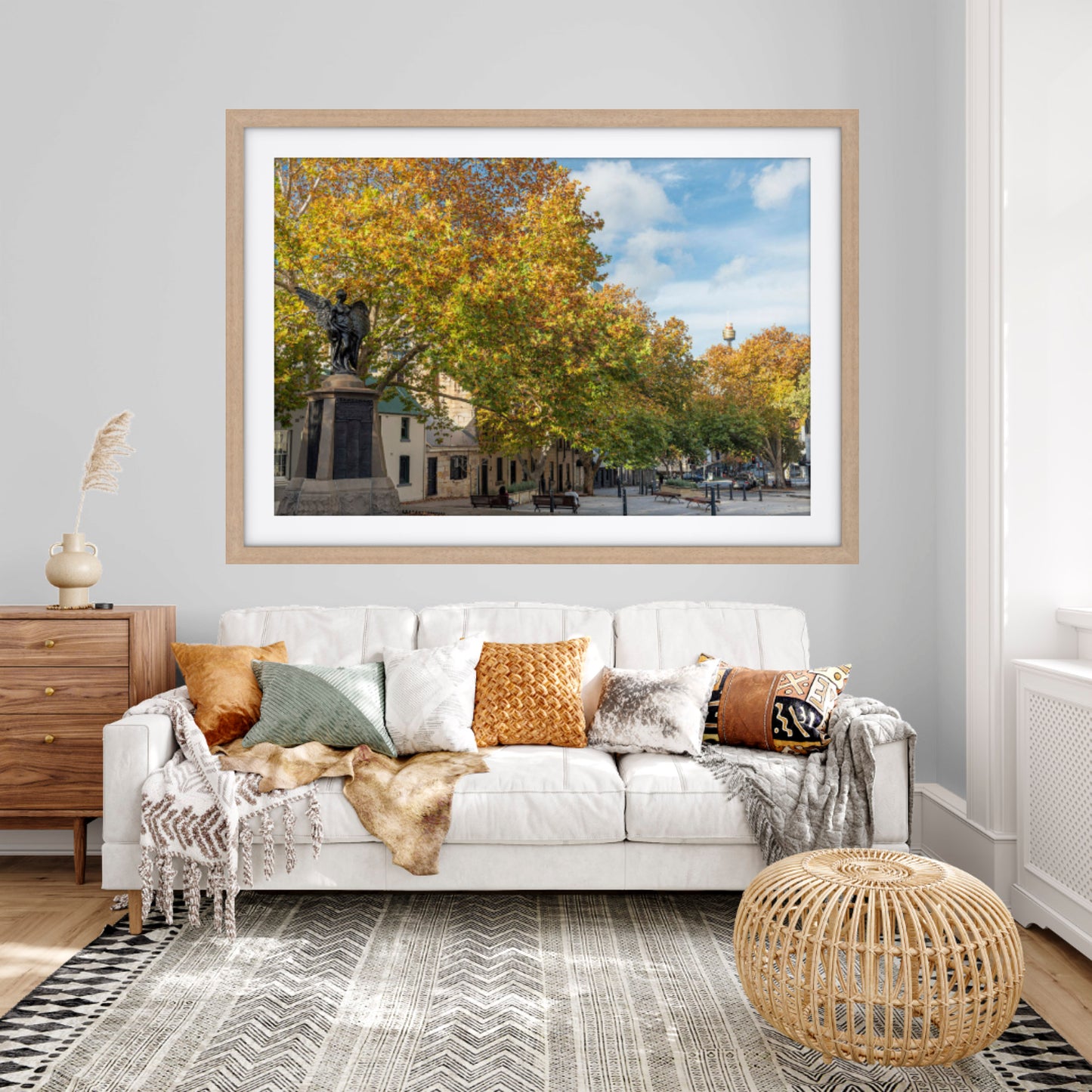 Living room with a framed picture of a park on the wall above a white sofa.