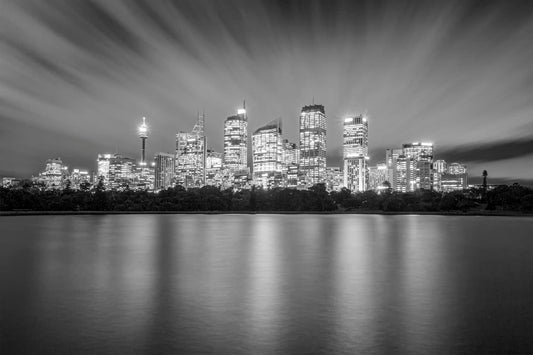 Black and white long exposure photograph of Sydney CBD at dusk with cirrus clouds and reflections in Farm Cove harbour water
