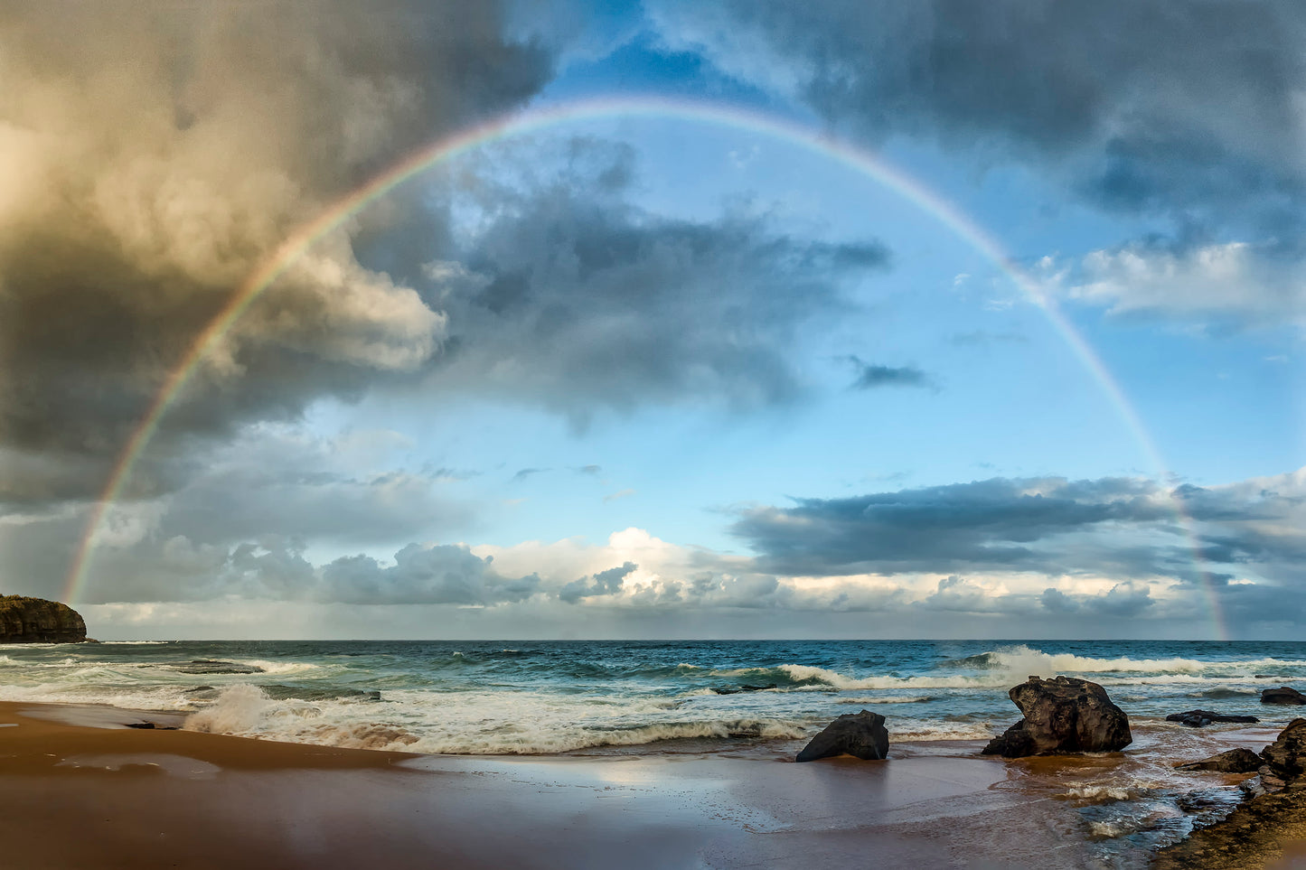 Rainbow over Turimetta Beach Sydney northern beaches with dramatic rock formations and stormy sky