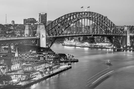 Black and white aerial photograph of Circular Quay with arcing ferry light trails mirroring Sydney Harbour Bridge from above