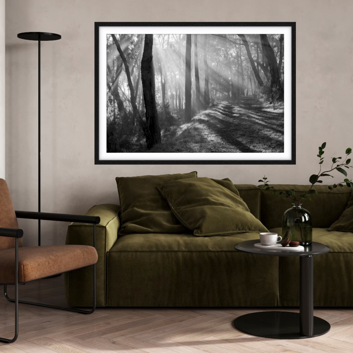 A framed black and white fine art forest print in a living room, with a green couch.