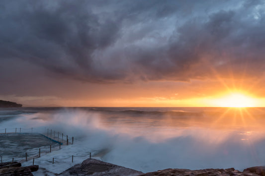 Dramatic wave crashing over South Curl Curl Rock Pool Sydney at sunrise with dark blue water and golden light