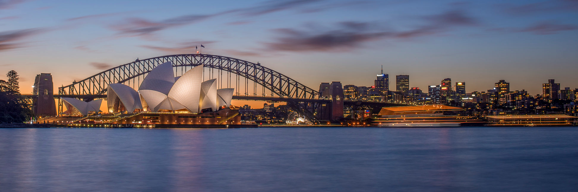 Color long exposure photograph of Sydney Harbour Bridge at blue hour with two boat light trails diverging paths