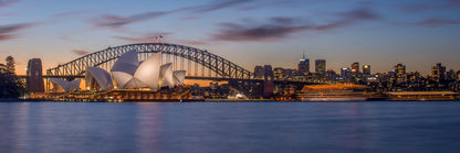 Color long exposure photograph of Sydney Harbour Bridge at blue hour with two boat light trails diverging paths