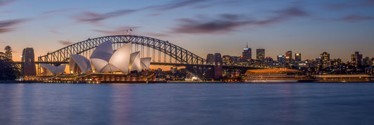 Color long exposure photograph of Sydney Harbour Bridge at blue hour with two boat light trails diverging paths