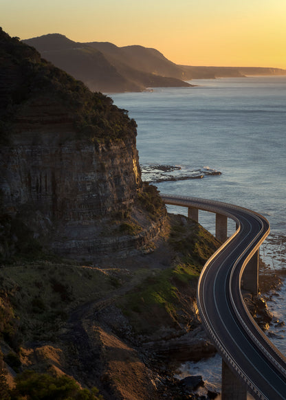 Sea Cliff Bridge Grand Pacific Drive NSW at sunrise with serpentine architecture above crashing ocean waves