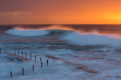 Rolling wave at South Curl Curl Rock Pool Sydney at sunrise with golden light and blue ocean water