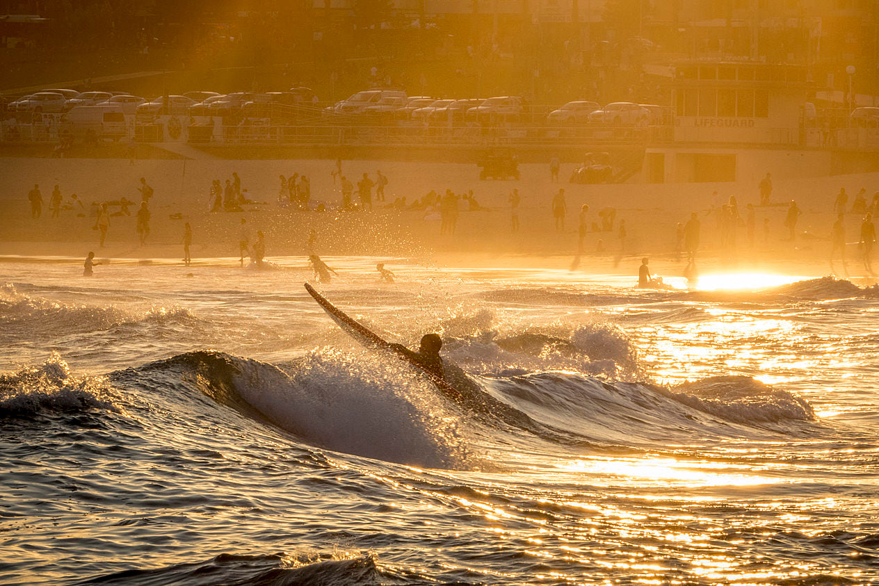 Surfer paddling out at Bondi Beach Sydney at sunset with golden amber light on water