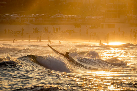 Surfer paddling out at Bondi Beach Sydney at sunset with golden amber light on water