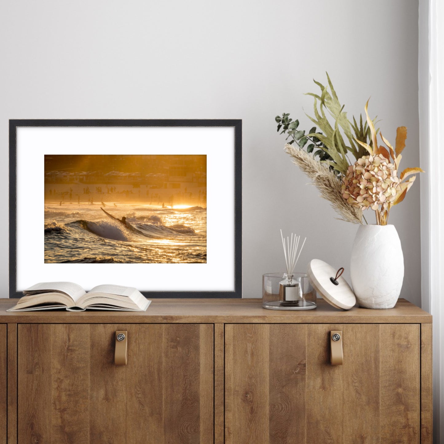 Framed artwork of a surfer paddling out at Bondi Beach on a wooden sideboard.